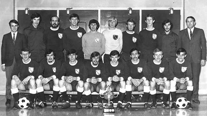 A team photo of the men’s varsity soccer team with some sitting and standing in their uniforms